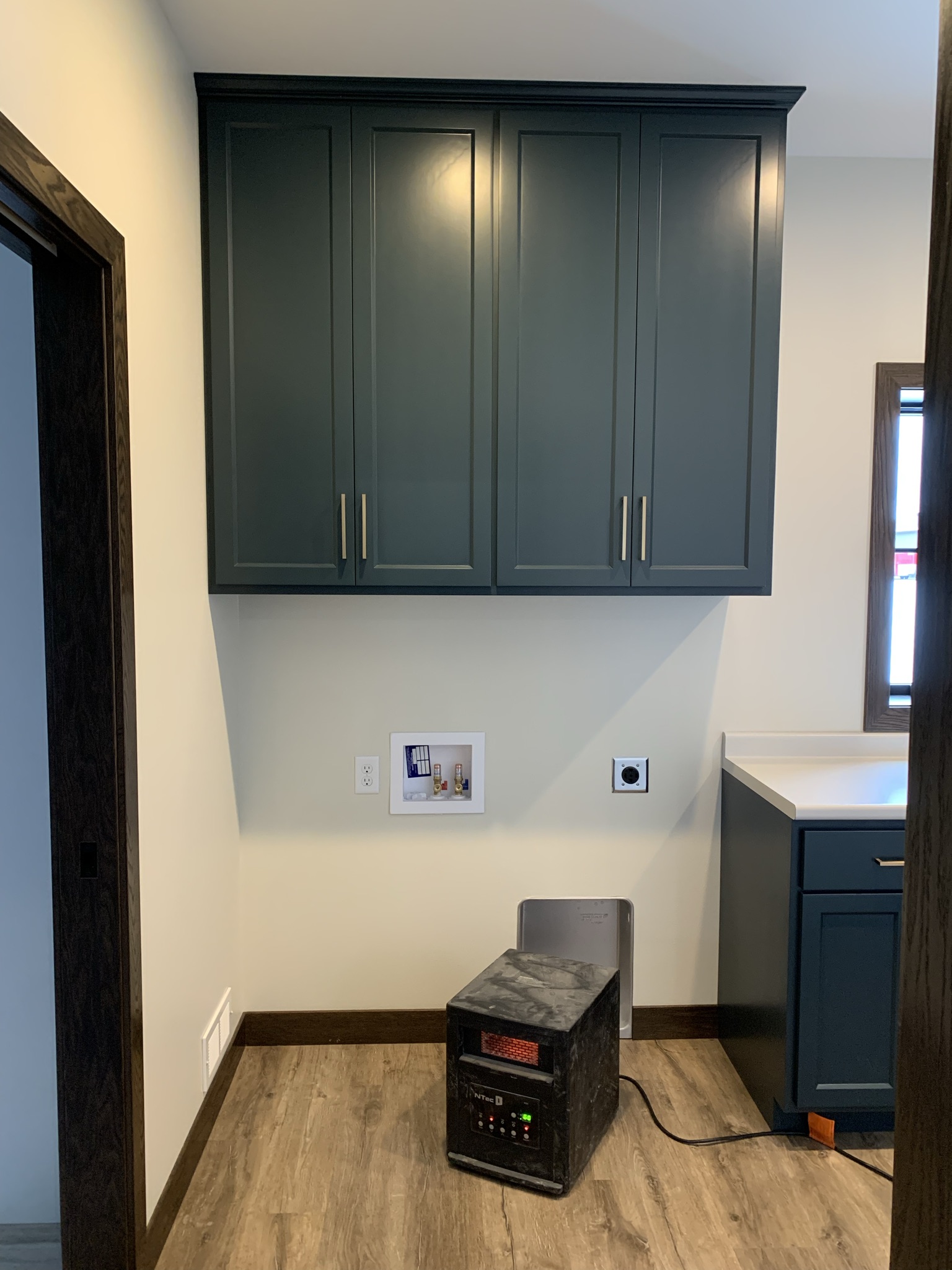 Wood-floored room with dark teal cabinets, white walls, and a countertop. A portable heater is on the floor. Bright, organized, modern space.