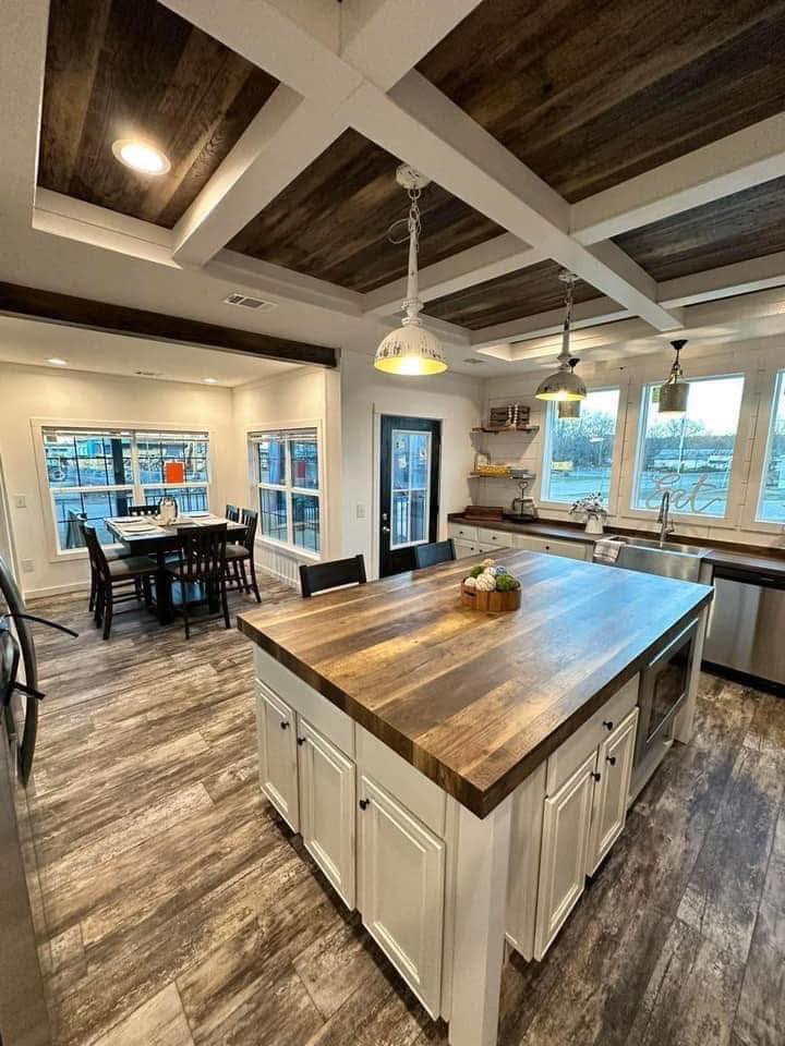 Spacious kitchen with rustic wood ceiling and flooring. Features a large island with a farmhouse-style countertop, pendant lights, and a dining area.