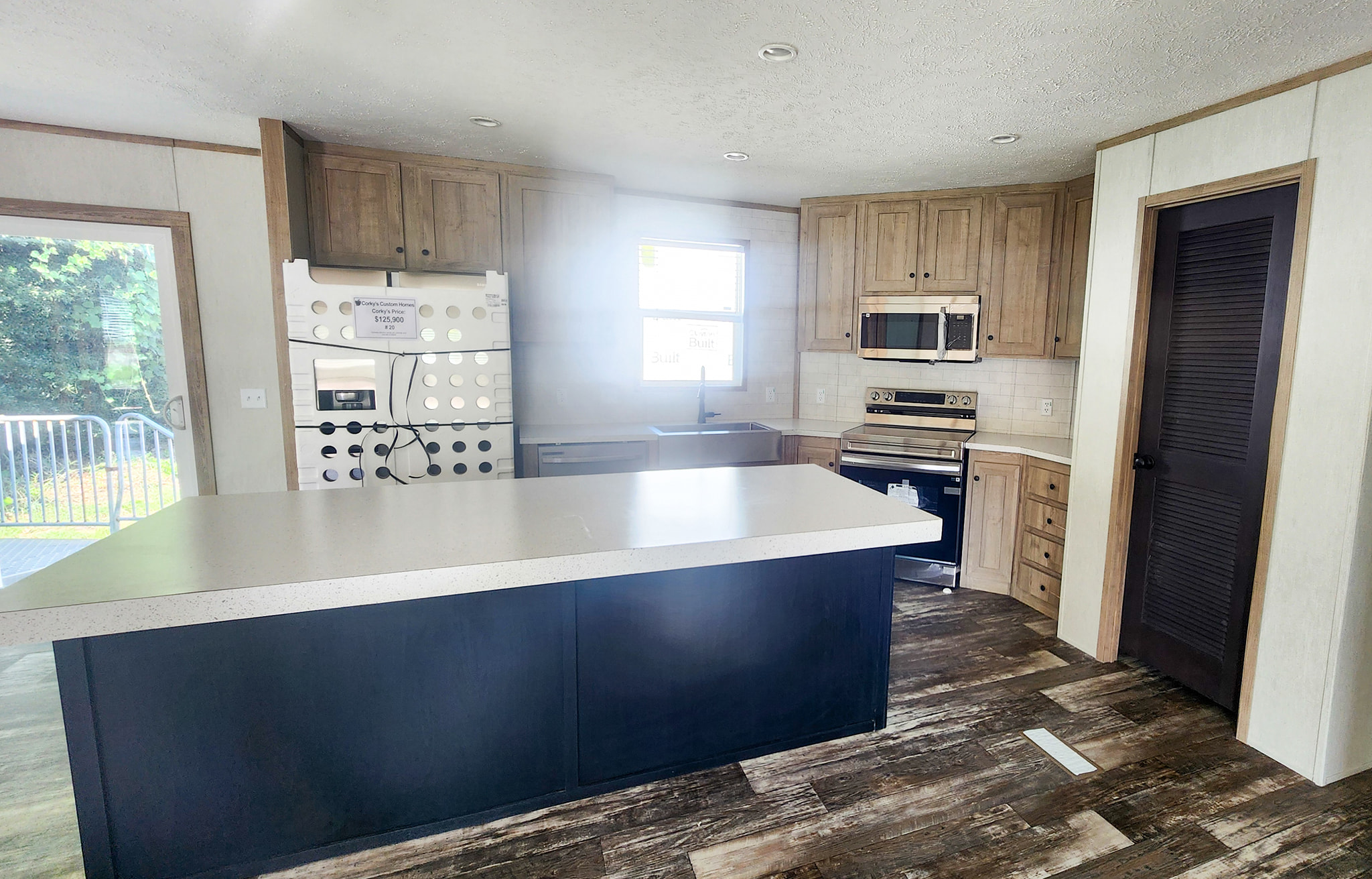 Modern kitchen with wood cabinetry, stainless steel appliances, and wide island counter. Sunlight streams through a window, creating a warm ambiance.