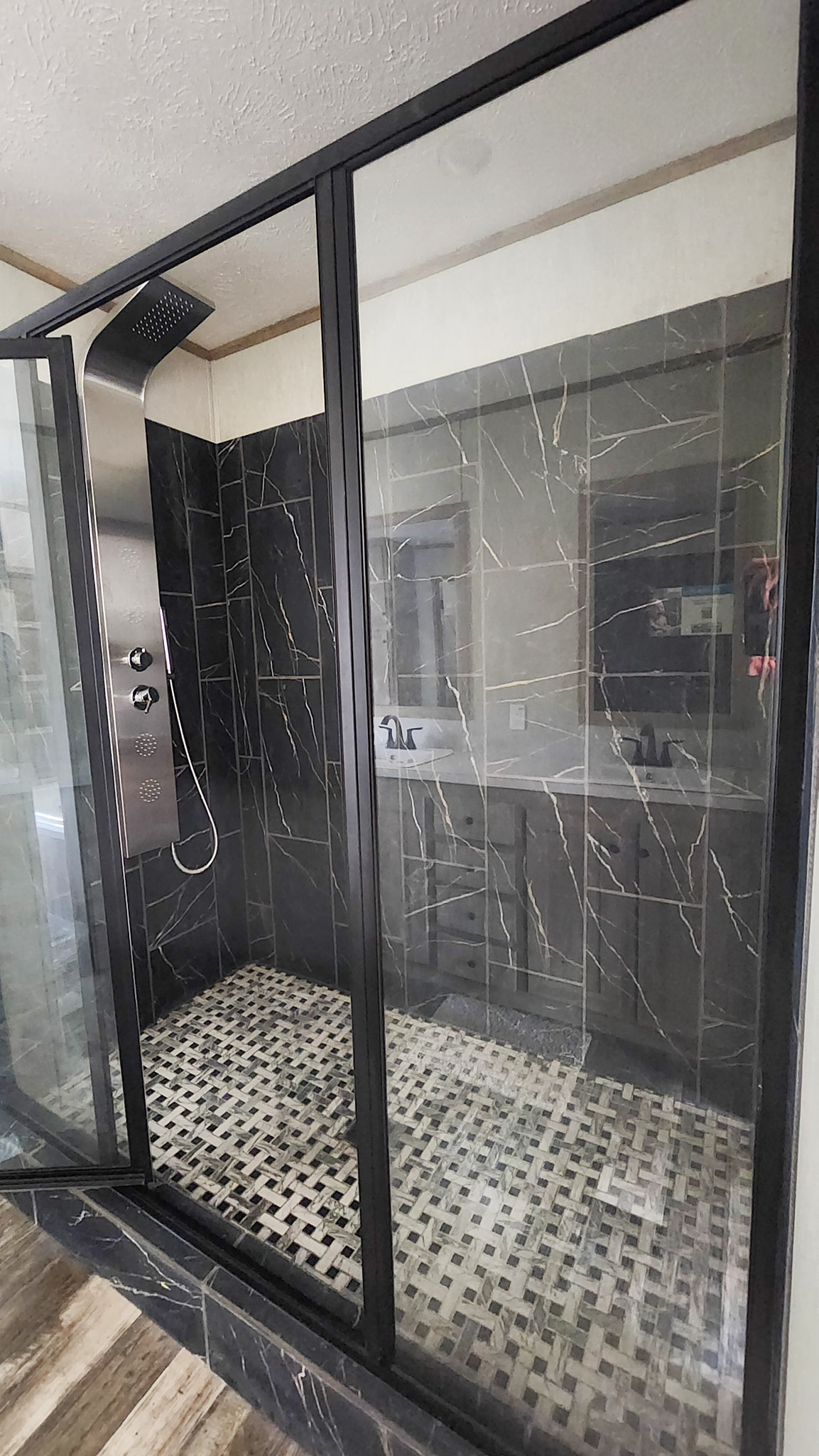 Modern shower with black marble walls, stainless steel shower panel, and glass door. The floor features a mosaic tile pattern. A sleek, contemporary feel.