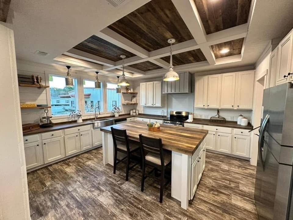 Spacious kitchen with white cabinets, dark wooden countertops, and an island. Pendant lights and a rustic wood ceiling create a cozy, elegant feel.