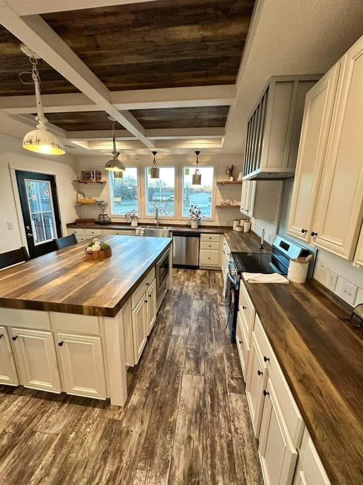 Modern kitchen with wooden countertops, white cabinets, and a large island. Three windows provide natural light, creating a warm and inviting atmosphere.