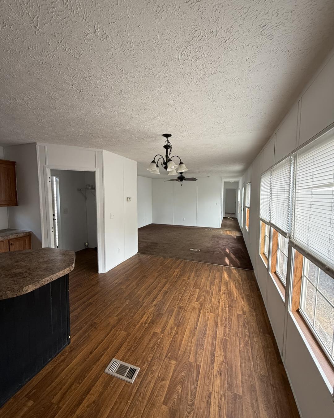 Spacious room with wooden and carpeted flooring, white walls, and large windows. A ceiling fan with lights hangs above, giving a bright and airy feel.