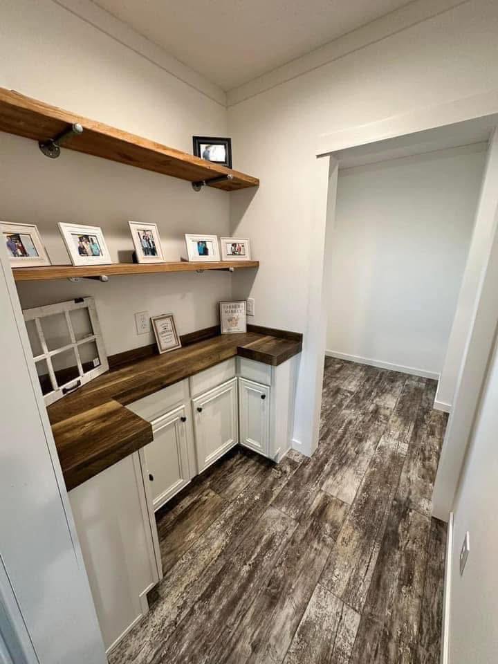 Narrow hallway with rustic wood flooring and counter. Two wooden shelves display framed photos. White cabinets below the counter add a cozy touch.