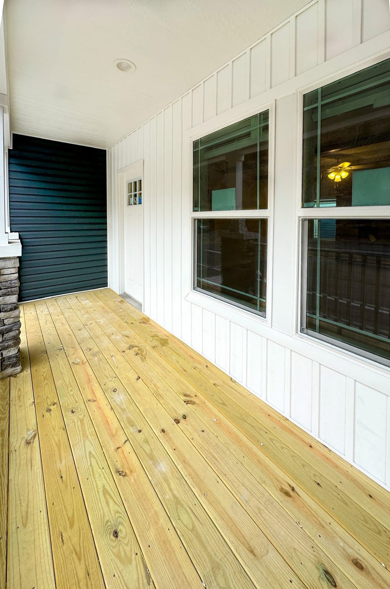 Front porch with a wood floor, white walls, and two large windows. It features a dark blue accent wall and a stone pillar, creating a modern, inviting feel.