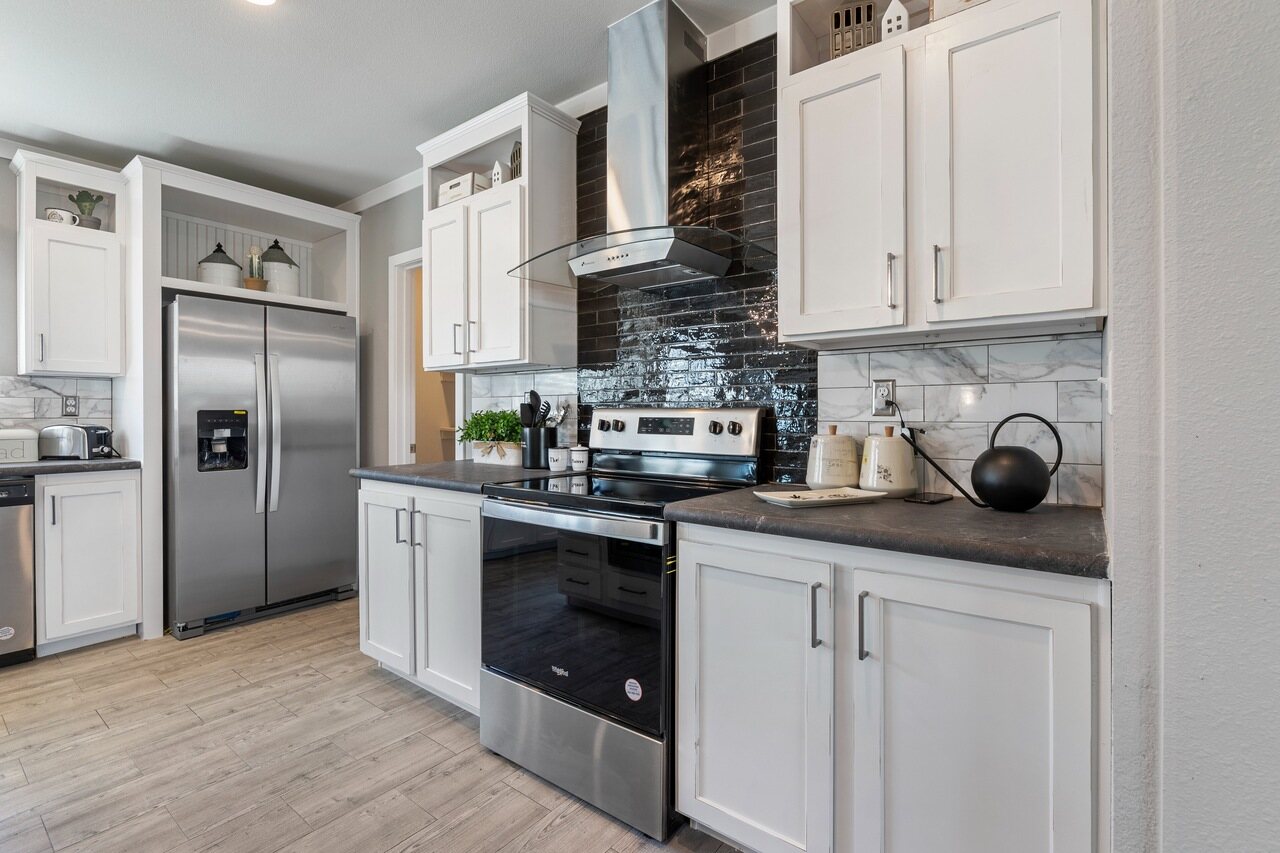 Modern kitchen with white cabinets, stainless steel appliances, and a black tile backsplash. Light wood flooring; a clean, sleek look.