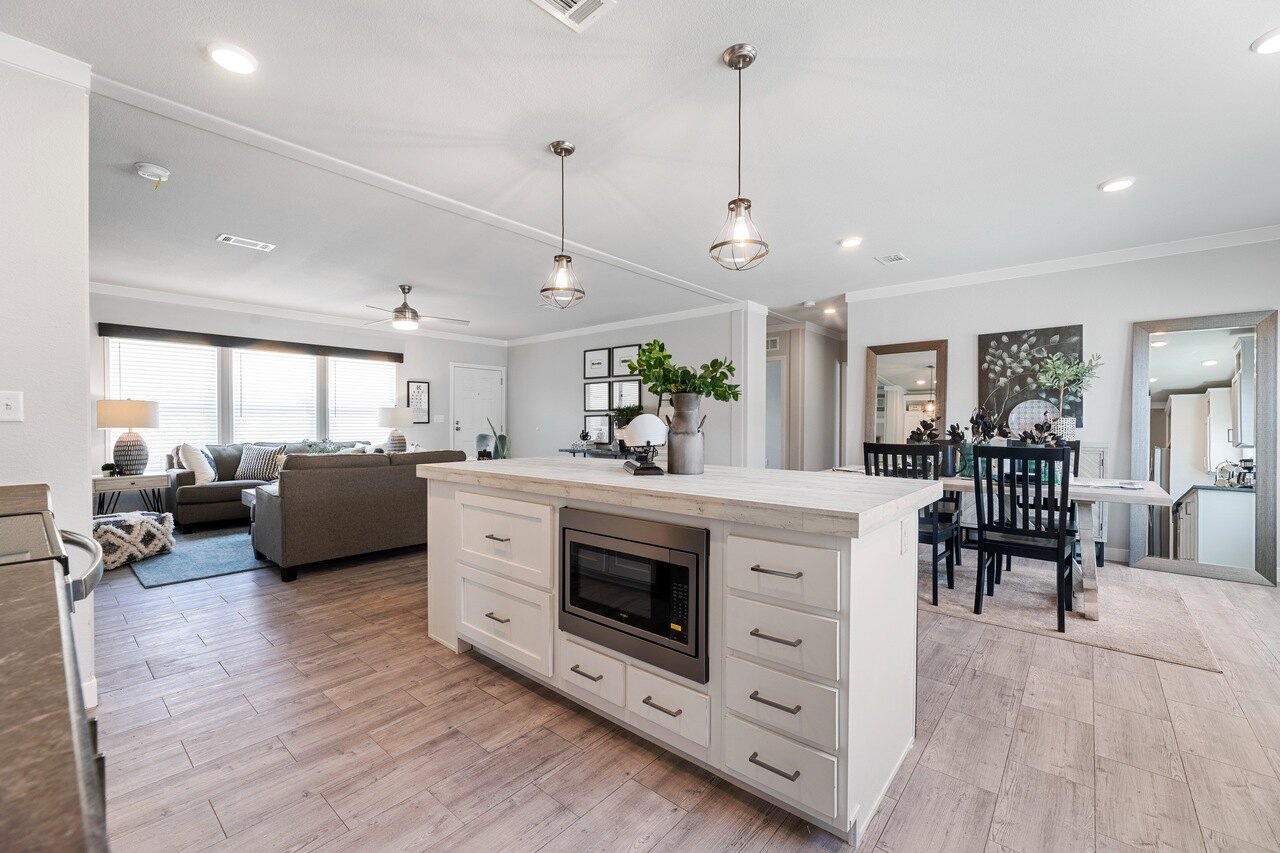 Modern open-concept kitchen and living room with white cabinetry, light wood floors, and cozy seating. Pendant lights and greenery add warmth.