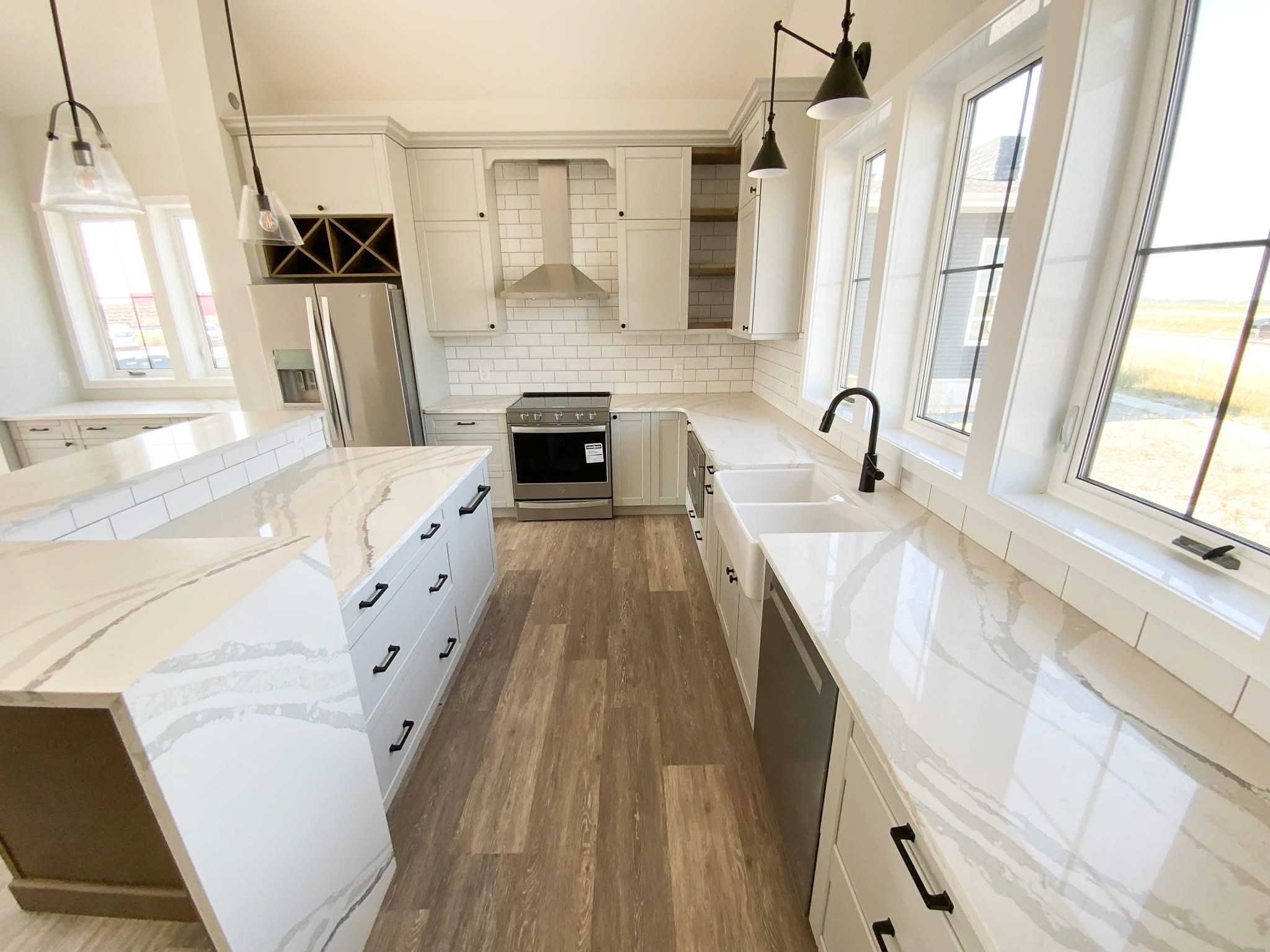 Bright, modern kitchen with light wood floors, white cabinetry, and marble countertops. Stainless steel appliances and pendant lights add elegance.