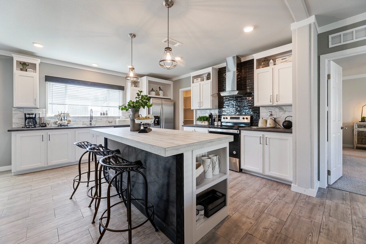 Spacious modern kitchen with a central island, light wood flooring, and sleek white cabinets. Black barstools and pendant lights add elegance.