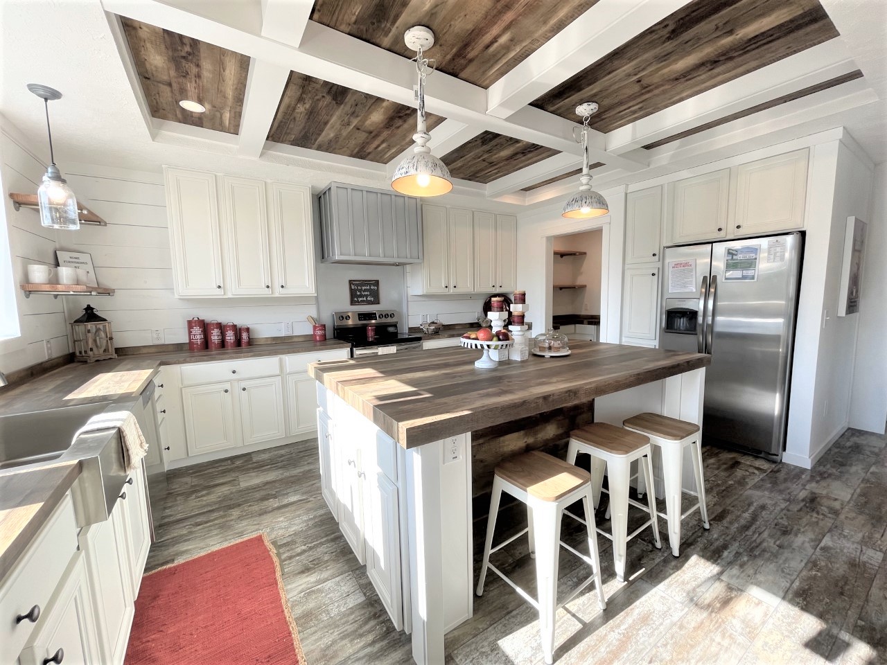 Bright farmhouse-style kitchen with a wood-accented ceiling, white cabinets, and a large island with stools. Stainless steel appliances add a modern touch.