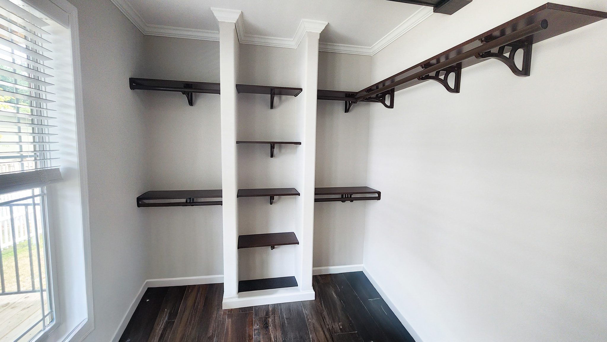 A minimalist room with white walls and dark wood flooring features built-in dark wood shelves on two walls, conveying a modern, organized tone.