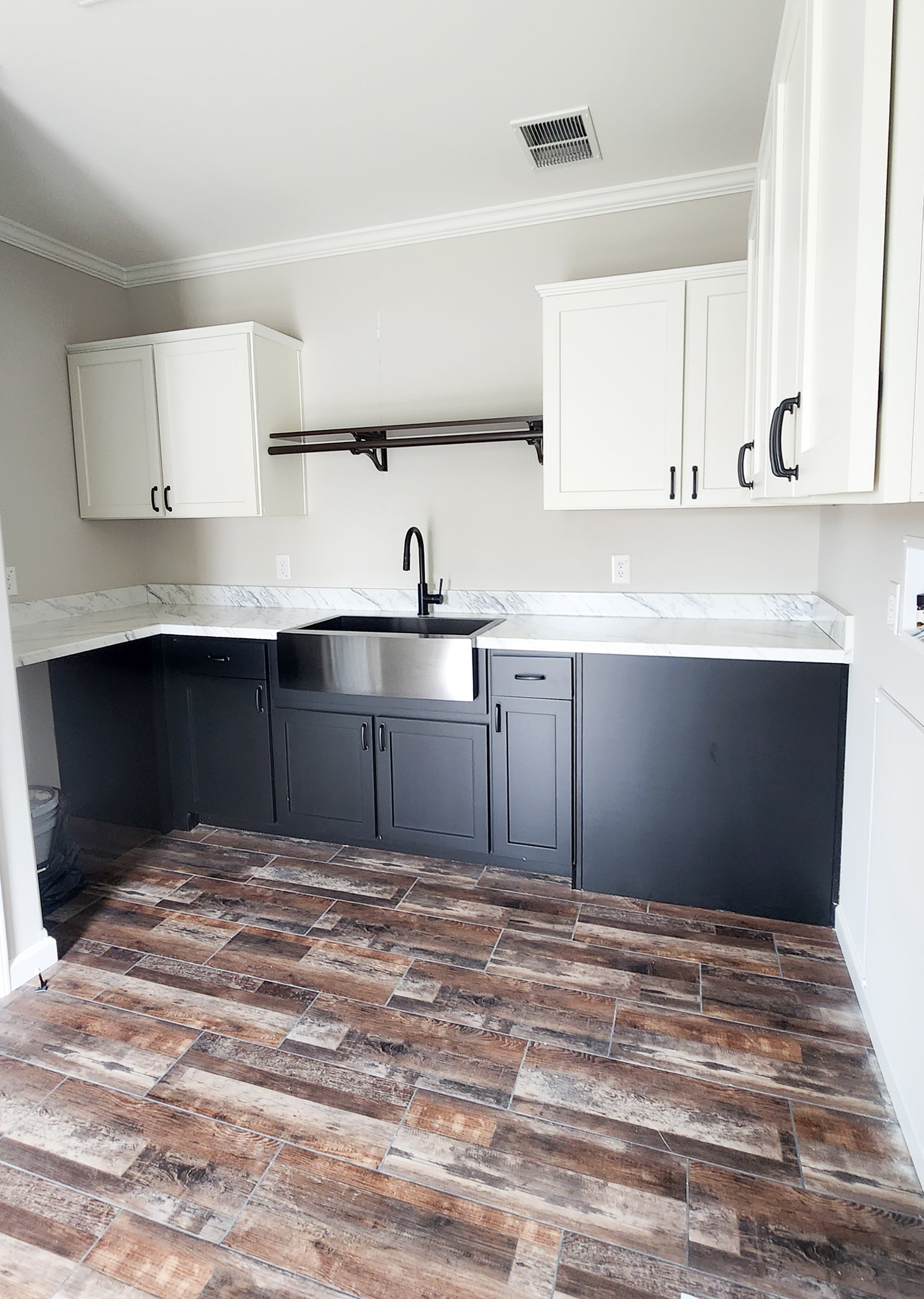 Modern kitchen with black and white cabinetry, a stainless steel farmhouse sink, marble countertops, dark faucet, and rustic wood-look tile flooring.