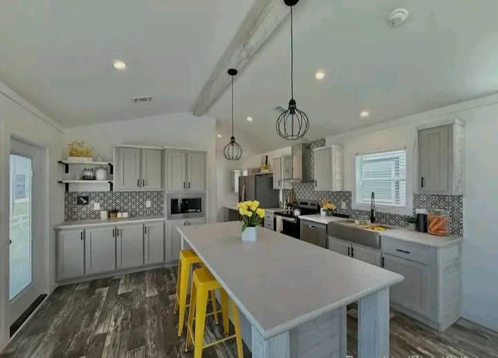 Bright kitchen with gray cabinets, patterned backsplash, and a central island. Yellow stools and decor add color. Pendant lights create a cozy feel.