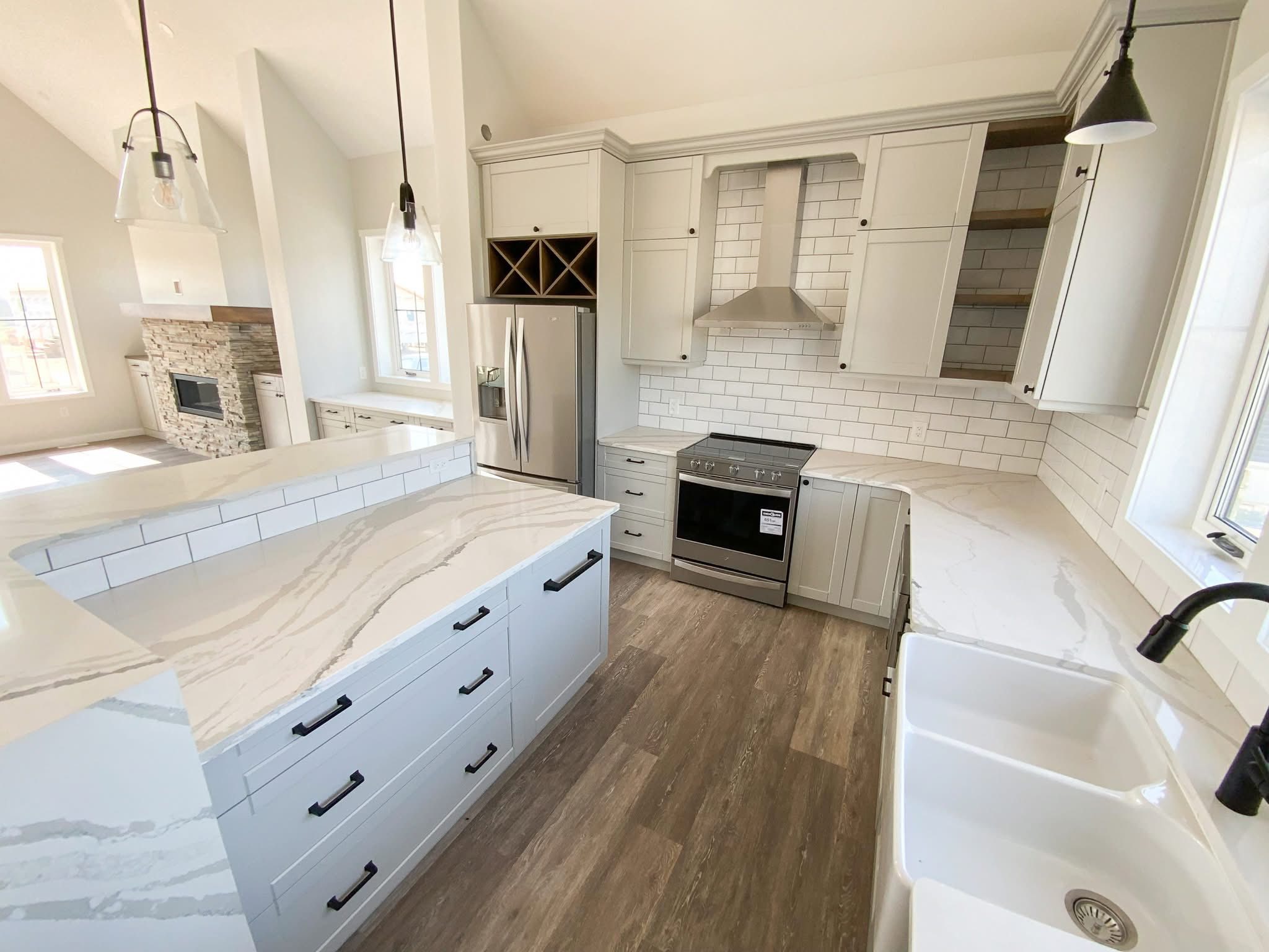 Spacious kitchen with white cabinets, marble countertops, subway tile backsplash, and stainless steel appliances. Rustic wood flooring adds warmth.