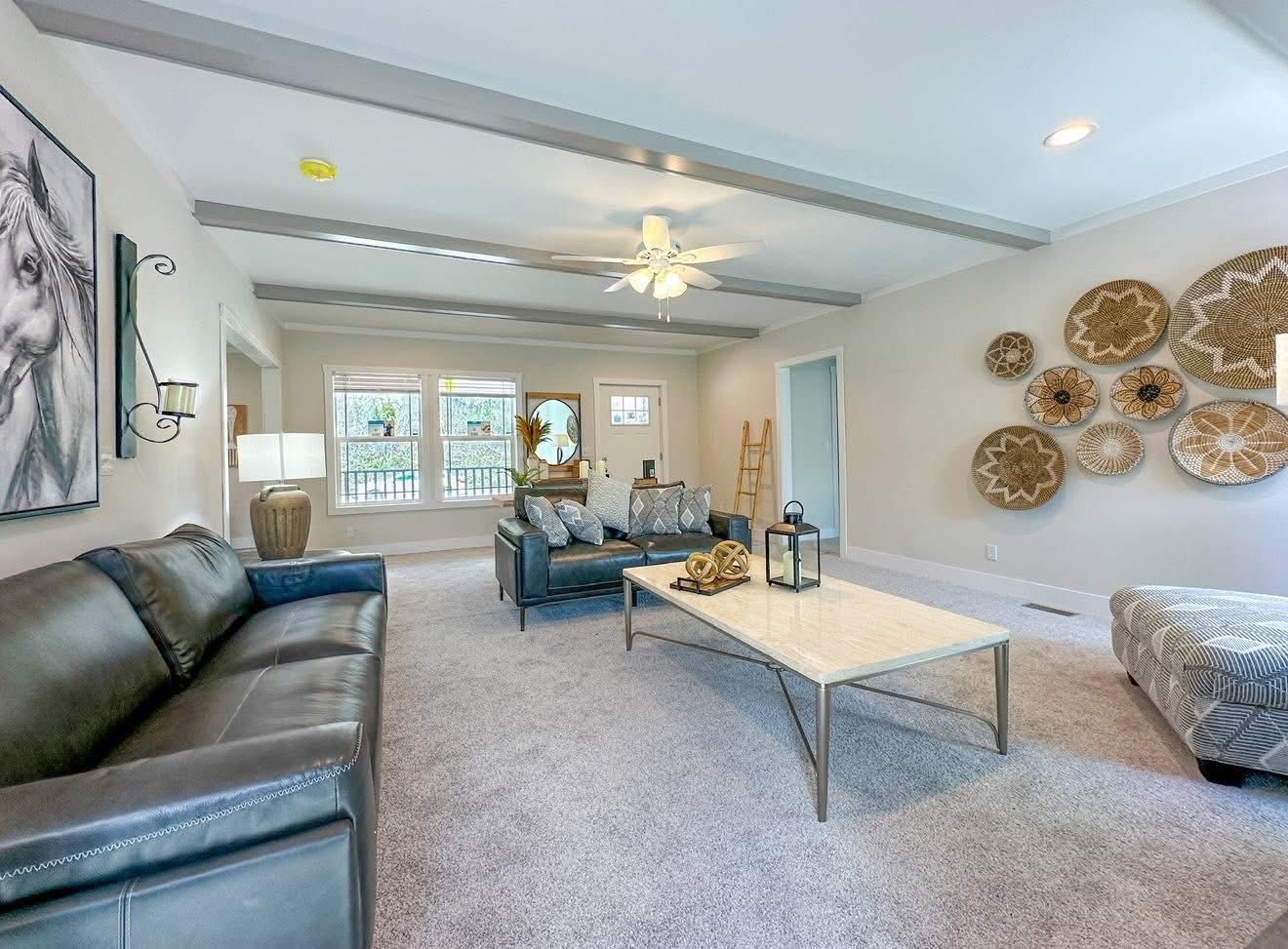 A cozy living room features gray sofas, a marble coffee table, and wall art with woven baskets. Bright sunlight enters through the large windows, creating a warm ambiance.