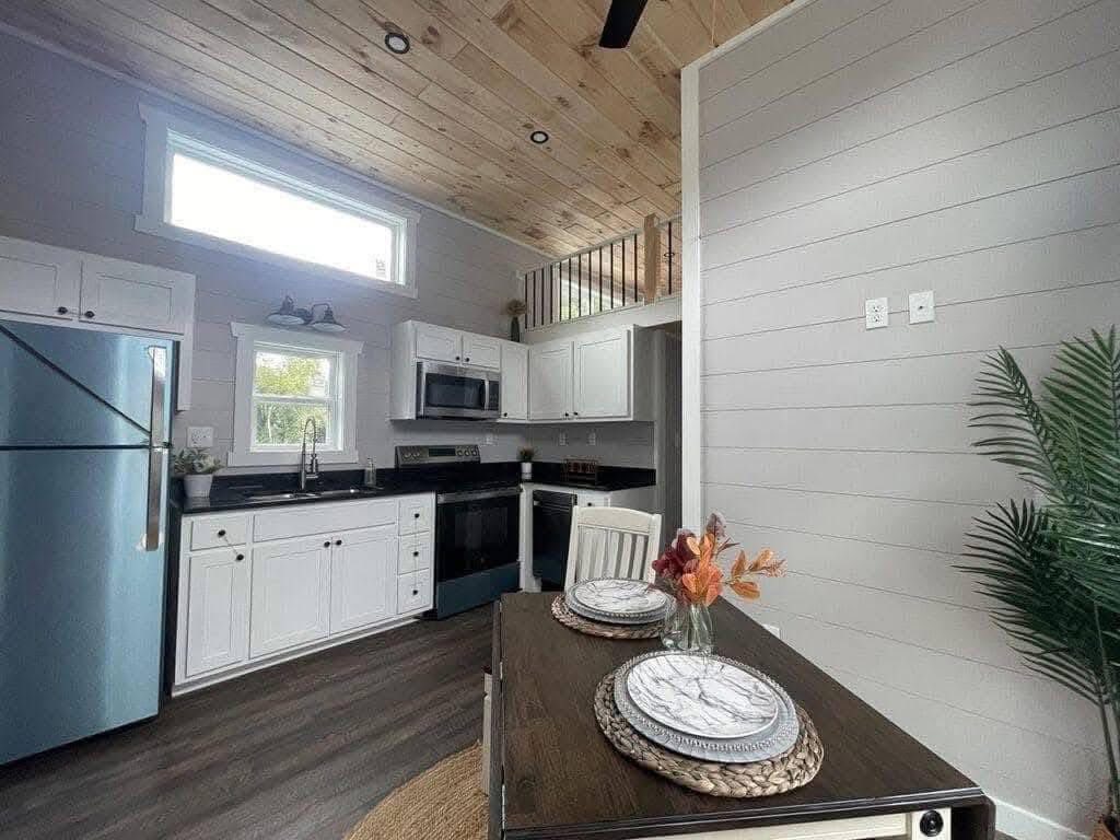 Cozy kitchen with white cabinets, dark countertops, and stainless steel appliances. A small dining table with plates and fall decor adds warmth.