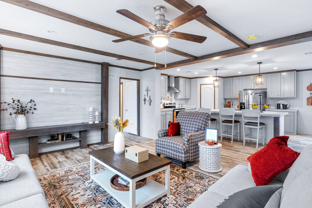 A modern living room with an open kitchen features a gray and red color scheme. Cozy seating, a wooden coffee table, and a decorative rug add warmth, while exposed beams and soft lighting enhance the inviting ambiance.