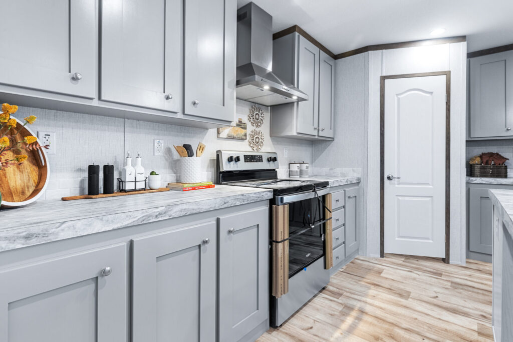Bright kitchen with gray cabinets, marble countertops, and stainless steel oven. Decor includes wooden tray and potted utensils. Warm, welcoming atmosphere.