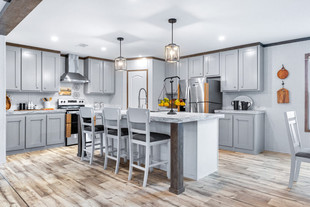Bright modern kitchen with gray cabinets and wood floors. An island with white chairs and pendant lights adds warmth. Stainless steel appliances accentuate the space.