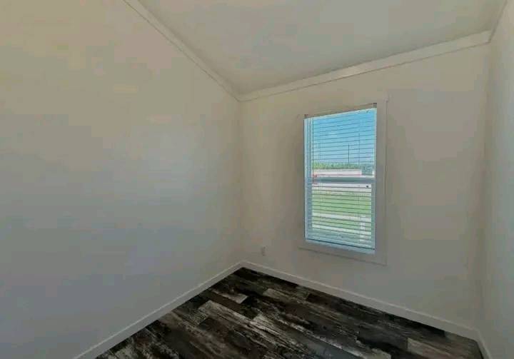 Small, empty room with white walls, a slanted ceiling, and a single window with blinds allowing soft daylight. Dark wood floor adds contrast.