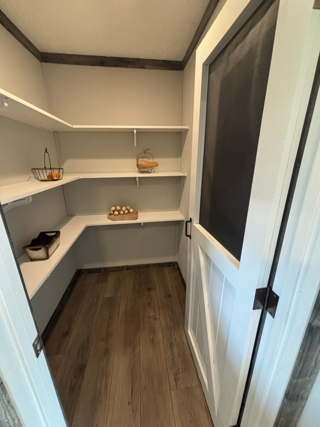 Cozy pantry with wood flooring and white shelves, featuring baskets of eggs, bread, and citrus fruits. A warm, rustic, organized space.