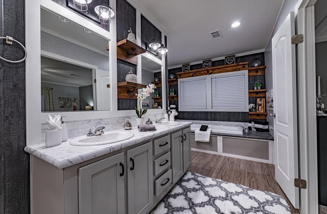 Spacious bathroom with dual sinks on a marble countertop, large mirrors, and wooden shelves. A bathtub sits under a window, creating a cozy, modern feel.