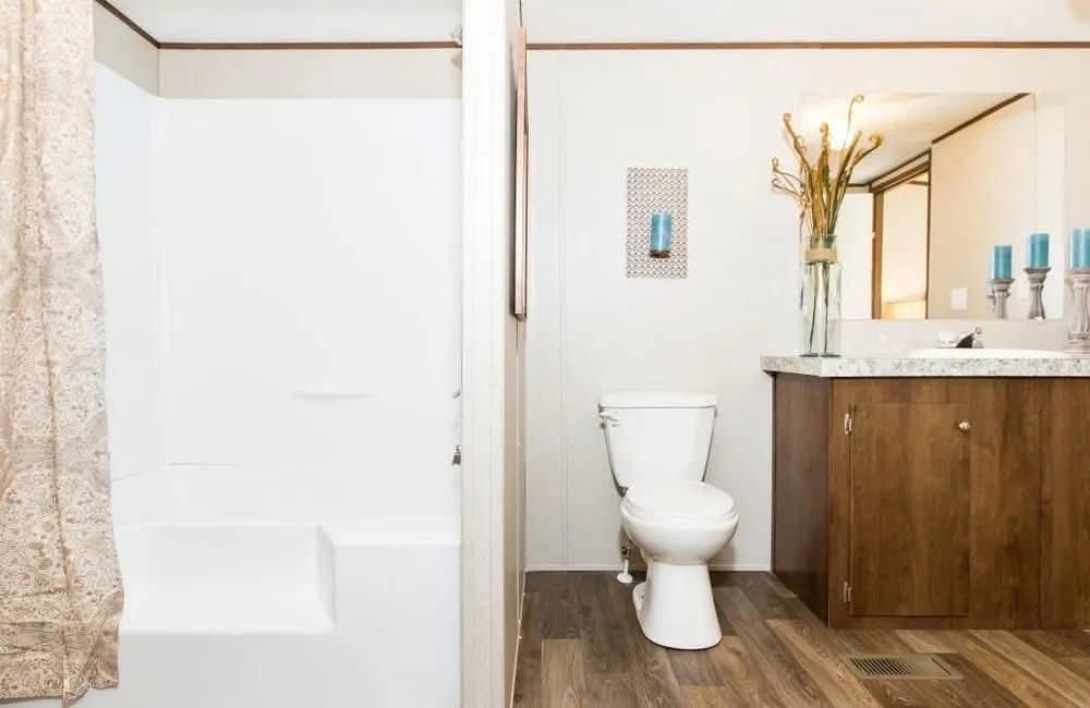 A modern bathroom featuring a white bathtub with a patterned curtain, a toilet, and a wooden vanity with candles and a vase, creating a serene and organized space.