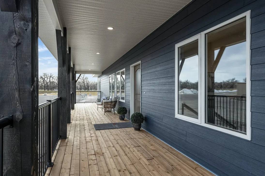 Wooden porch with a blue exterior, large windows, and small plants. A bench and table are near the door, creating a cozy, inviting atmosphere.