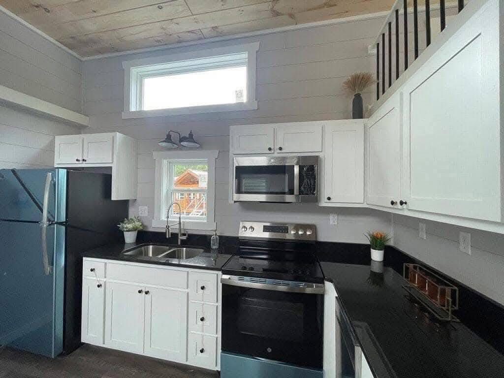 Modern kitchen with white cabinets, black countertops, and stainless steel appliances. A small window brings natural light, brightening the space.