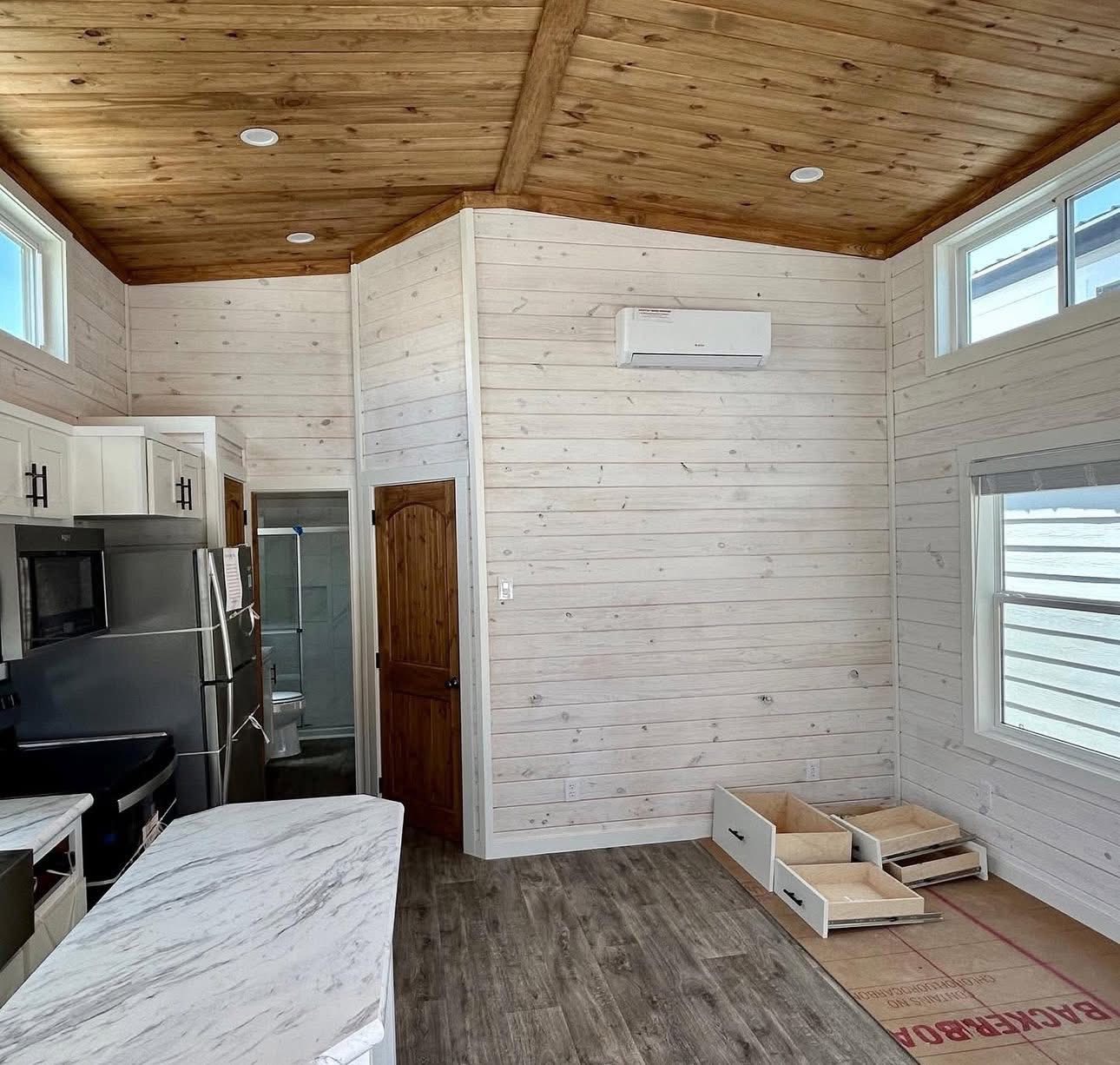 Spacious room with light wood walls and ceiling, marble countertop, and stainless steel fridge. Open storage drawers reveal an ongoing renovation.