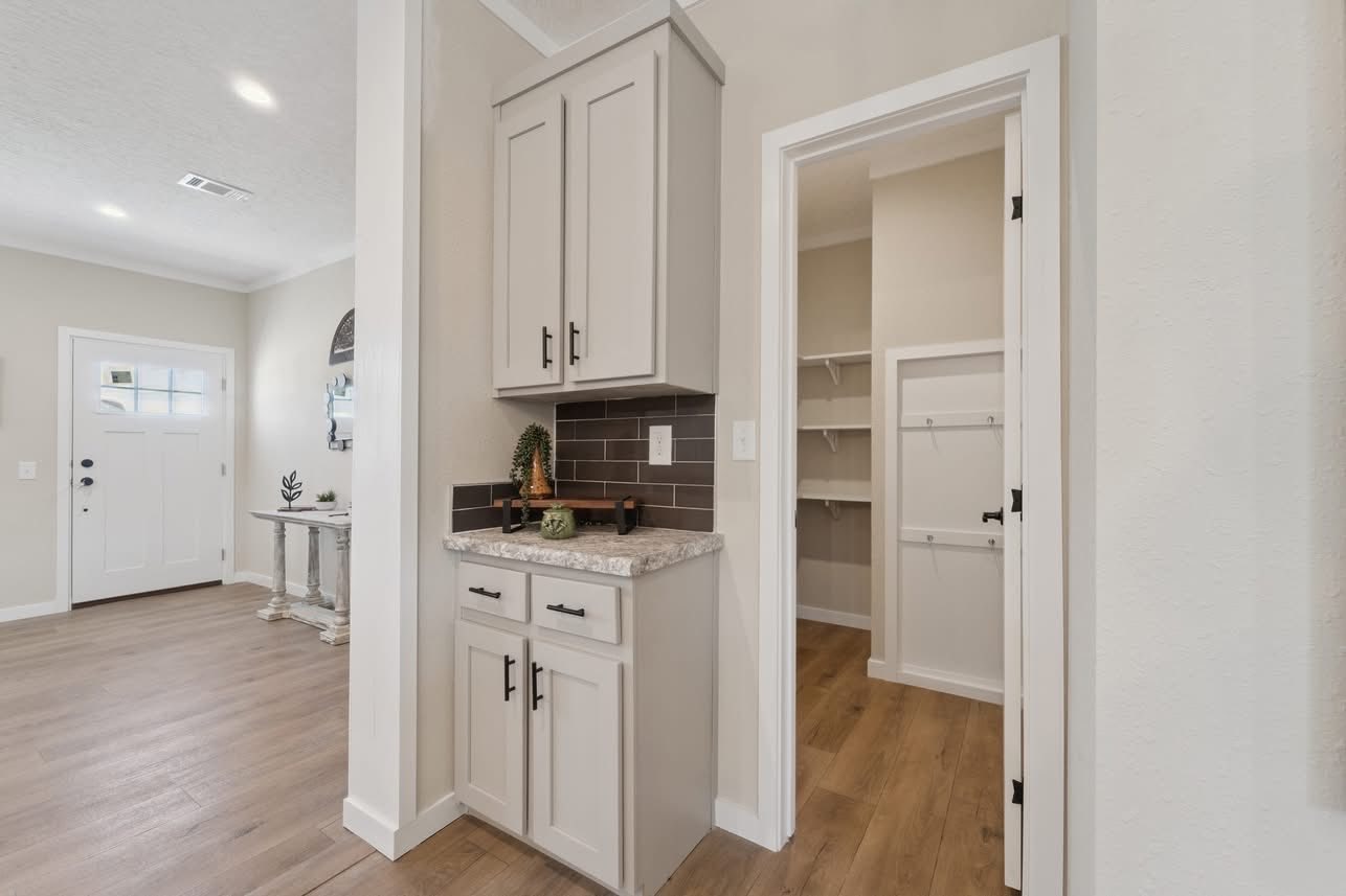 Bright entryway with hardwood floors and a white front door on the left. A small alcove features a beige cabinet and counter, leading to a closet.