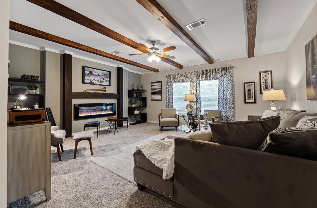 Cozy living room with wooden ceiling beams, sectional sofa, modern fireplace, elegant decor, and large windows with patterned curtains, creating a warm, inviting atmosphere.