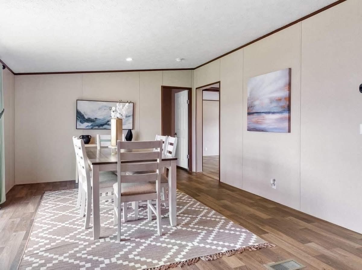 Minimalist dining room with a wooden table, six chairs on a geometric rug, and abstract paintings on beige walls. Bright and serene atmosphere.