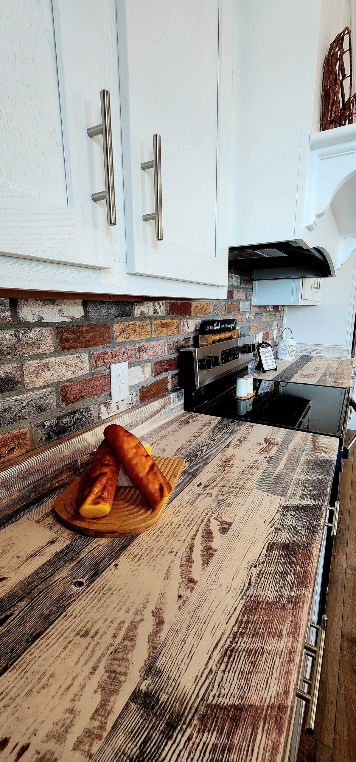 Rustic kitchen with textured brick backsplash, wooden countertops, and white cabinets. Triangular pastries on a wooden board create a cozy, inviting atmosphere.