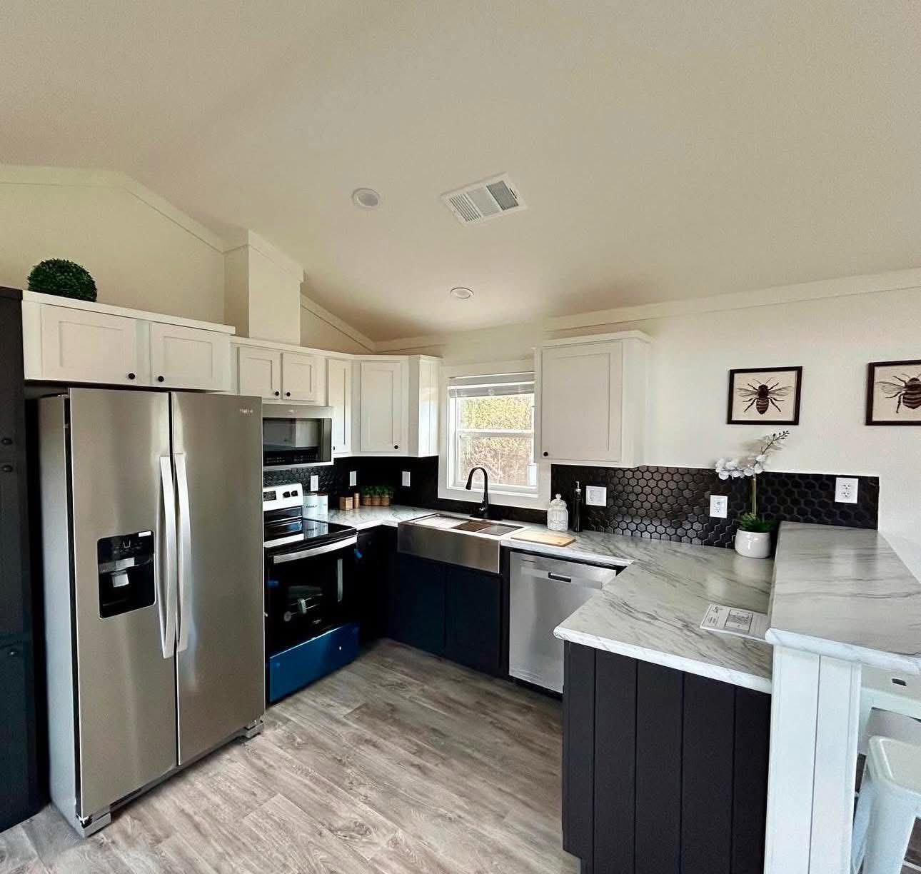 Modern kitchen with stainless steel appliances, white and black cabinetry, marble countertops, hexagonal tile backsplash, and insect art on the wall.