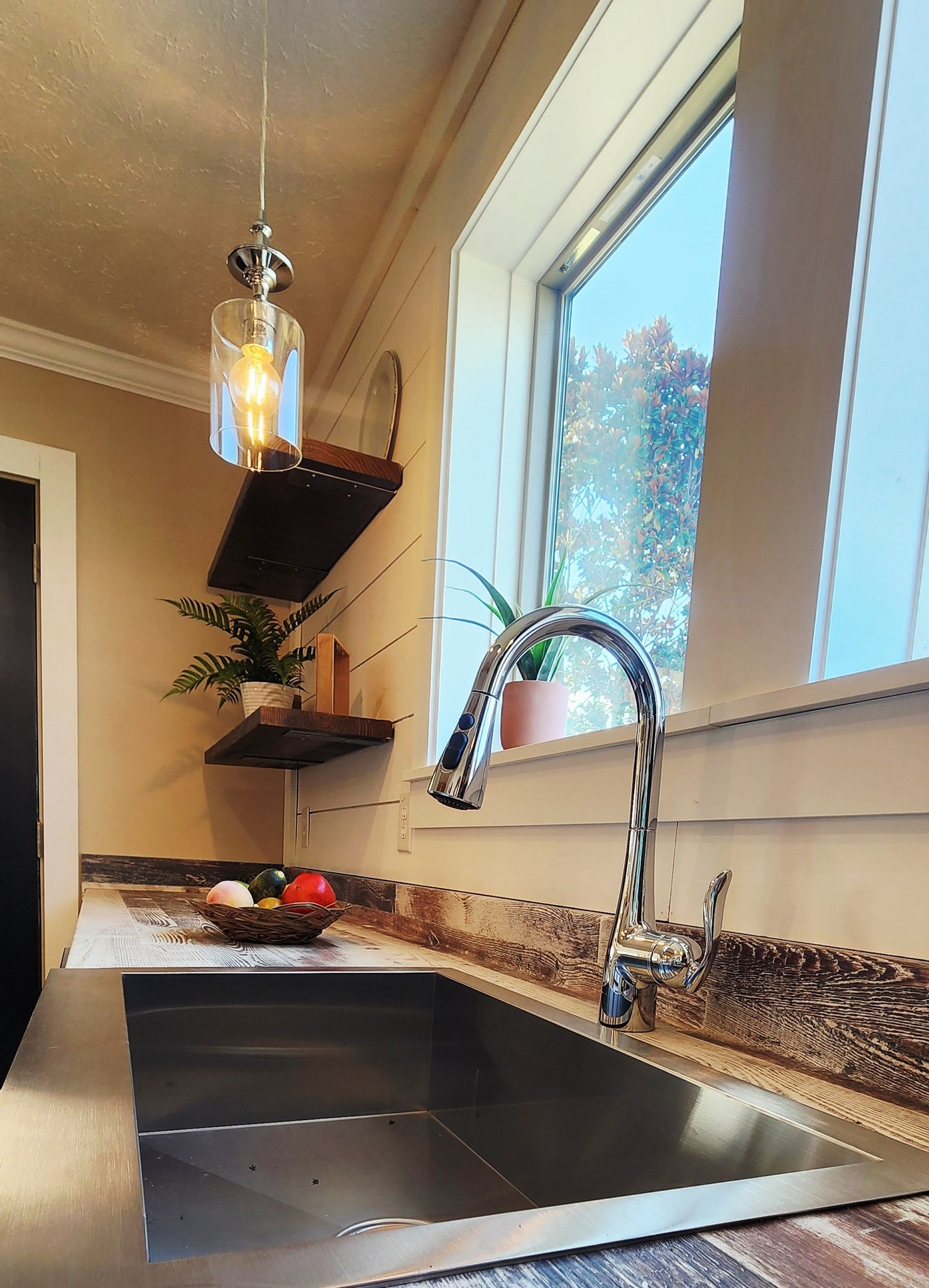 Modern kitchen sink with a sleek metal faucet, set in a rustic wooden counter. Warm lighting and potted plants create a cozy, inviting atmosphere.