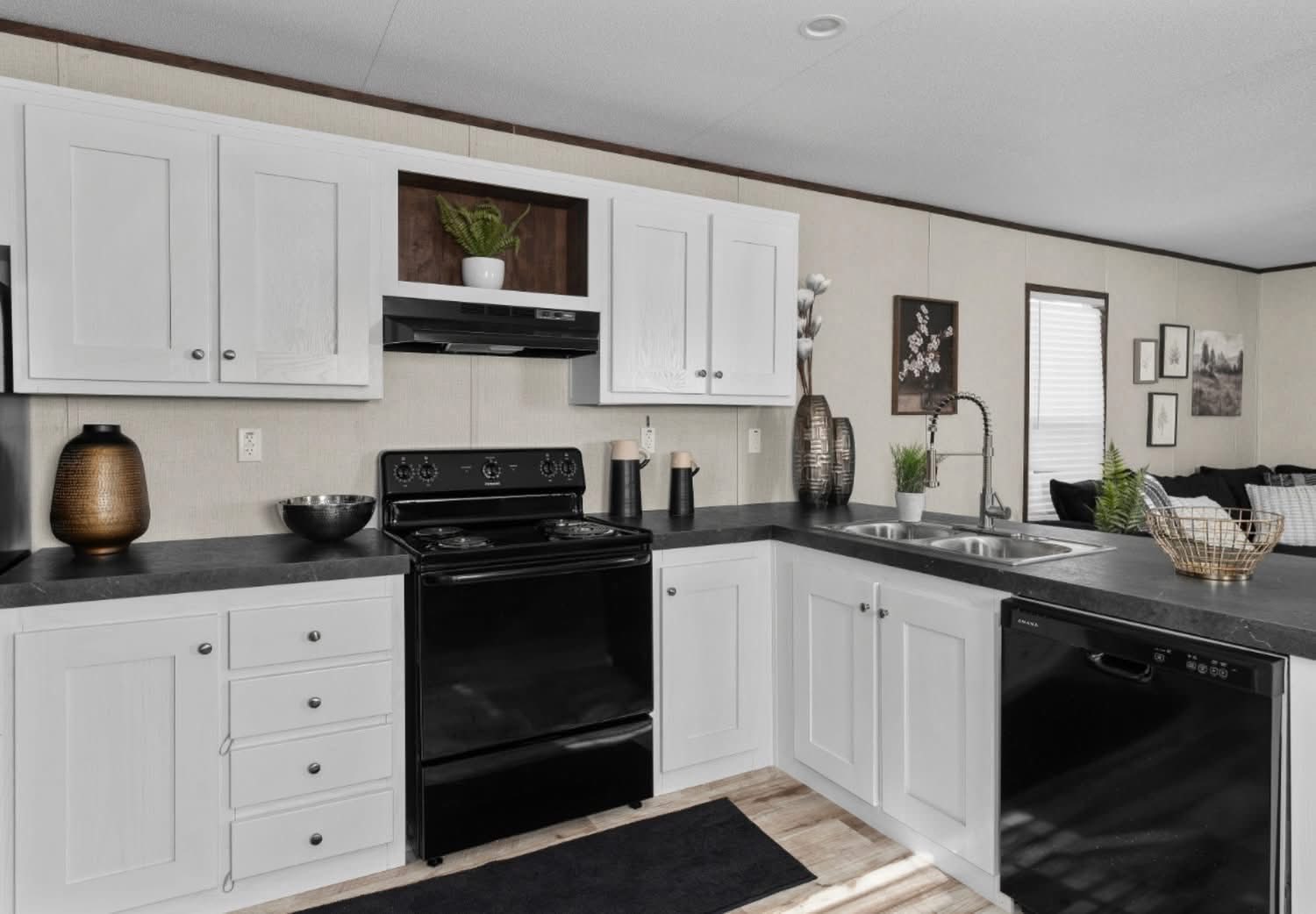 Modern kitchen with white cabinets and black appliances, including a stove and dishwasher. Decor includes plants and vases, creating a cozy feel.