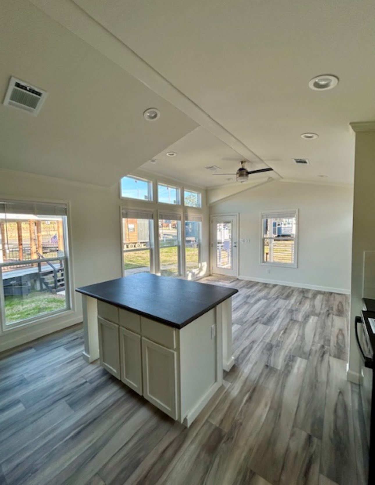 Spacious, sunlit room with high ceilings and large windows. Features a central island with dark countertop and wood-look flooring. Inviting and airy.