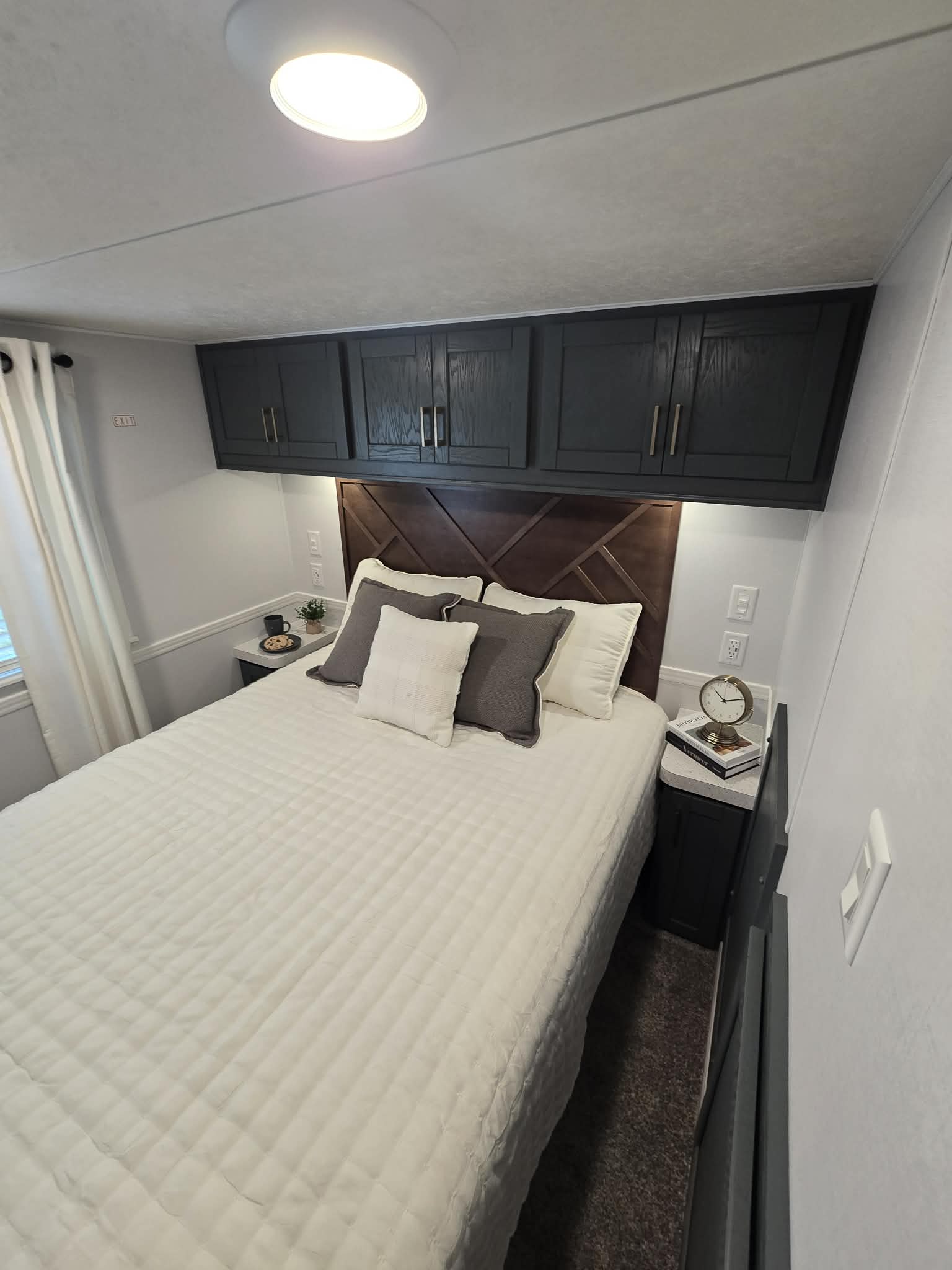 Cozy bedroom with a neatly made bed featuring white and gray pillows. Dark wood cabinets and a geometric headboard create a modern feel. Soft, ambient lighting enhances the calming ambiance.