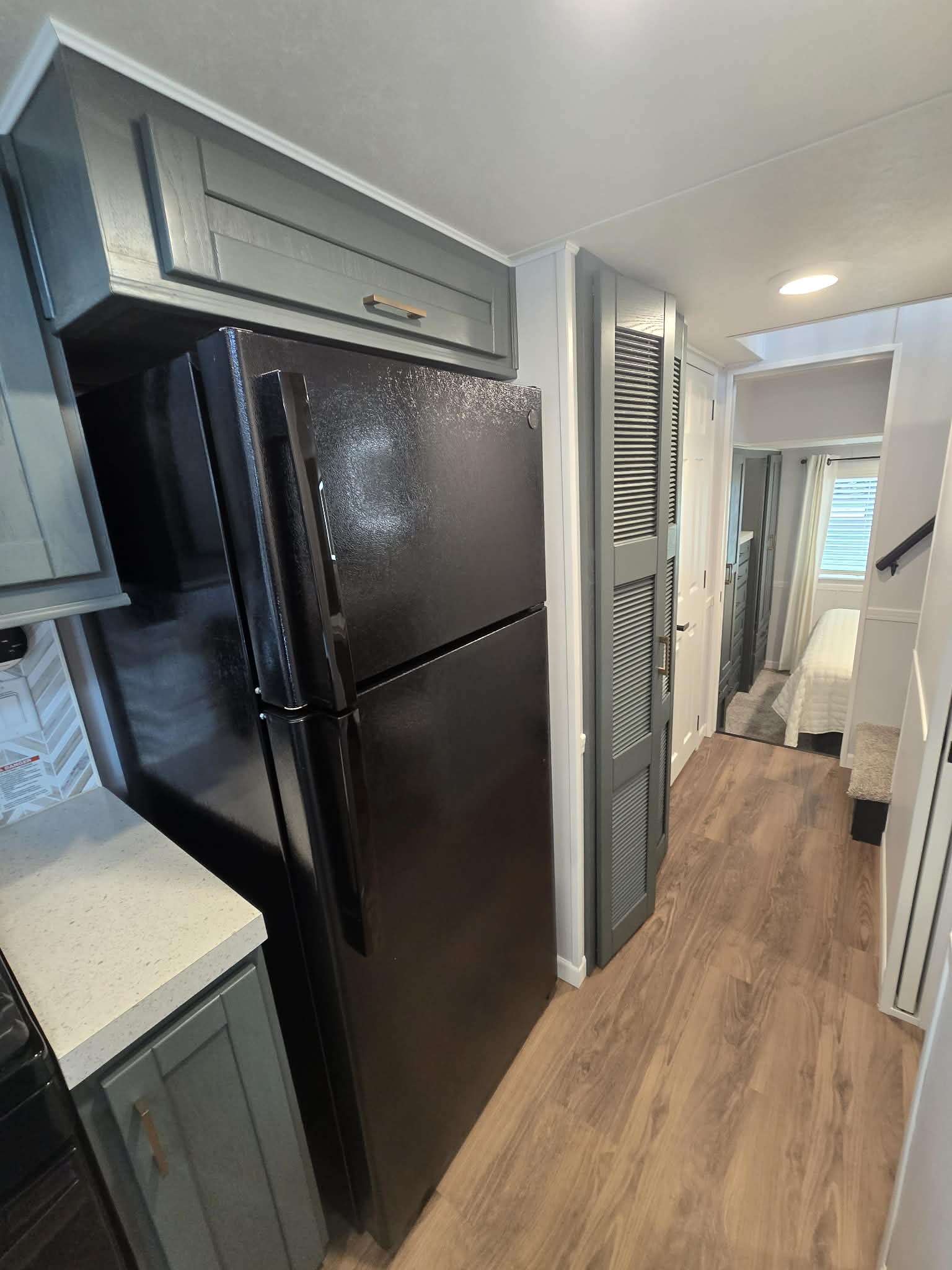 Modern tiny home interior with high ceiling and wood floors. Features a kitchen island, barstools, white sofa, recliner, and large windows. Cozy ambiance.