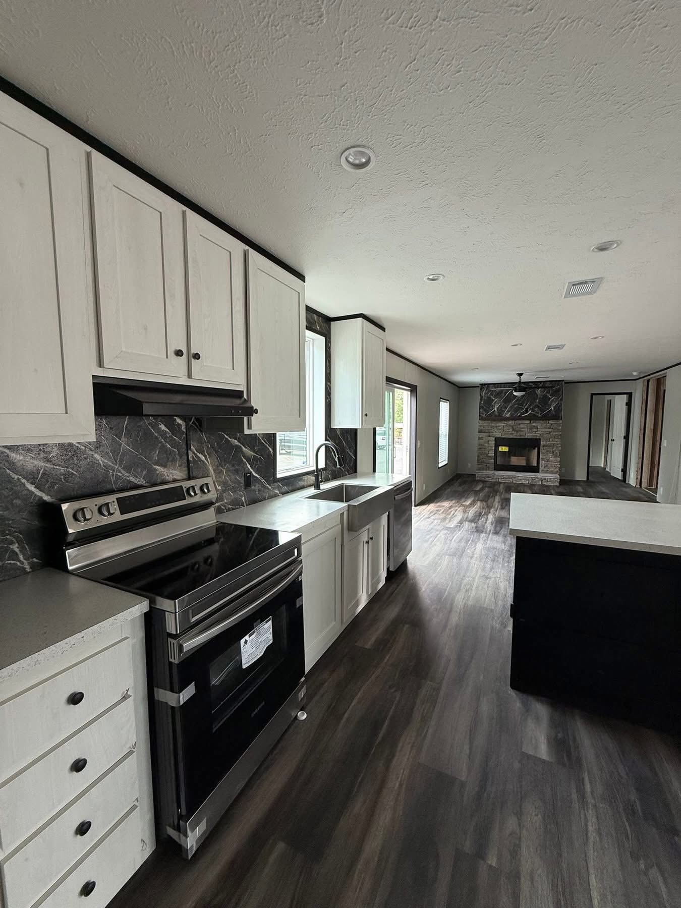 Modern kitchen and living area with dark wood floors, white cabinets, and a marble backsplash. A fireplace is visible in the background. Bright and sleek design.