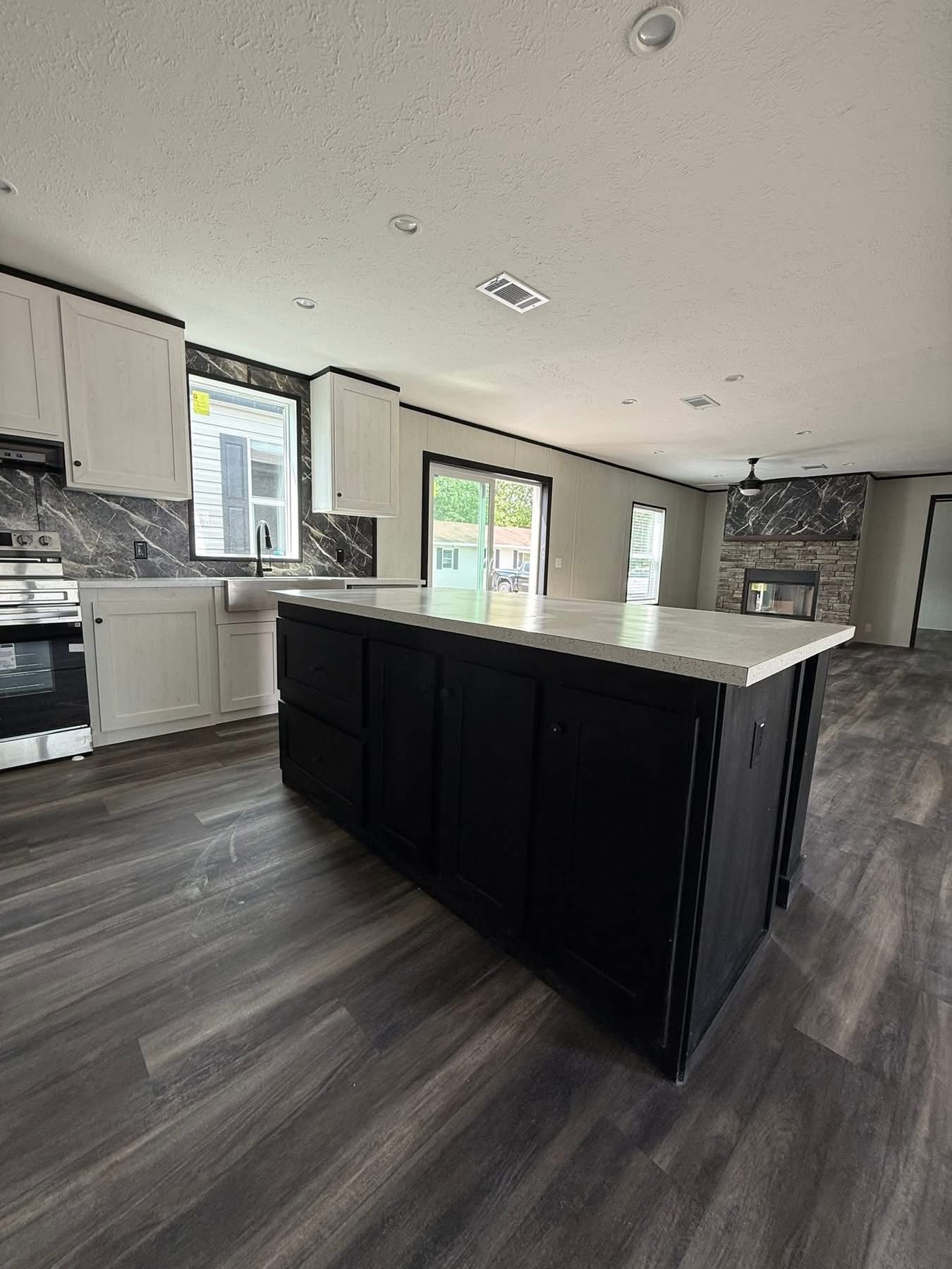 Modern kitchen with a black island and light countertop. White cabinets and stainless steel appliances are set against dark marble walls. Bright, airy atmosphere.