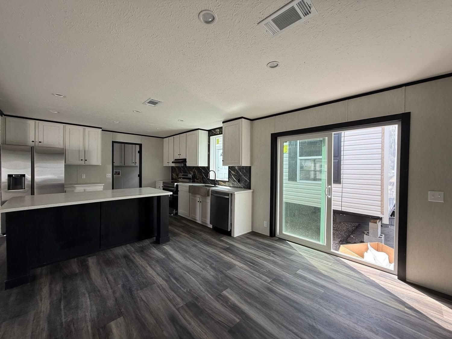 Modern kitchen with dark wood flooring, white cabinetry, stainless steel appliances, and a central island. A sliding glass door lets in natural light.
