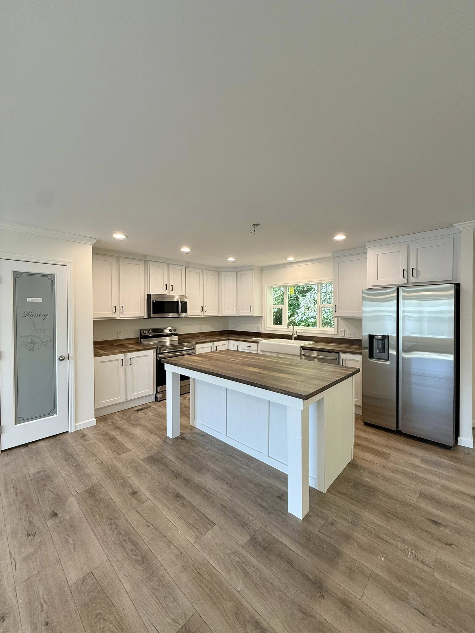Spacious kitchen with white cabinets, stainless steel appliances, and a wooden island. Natural light streams through large windows, creating a warm ambiance.