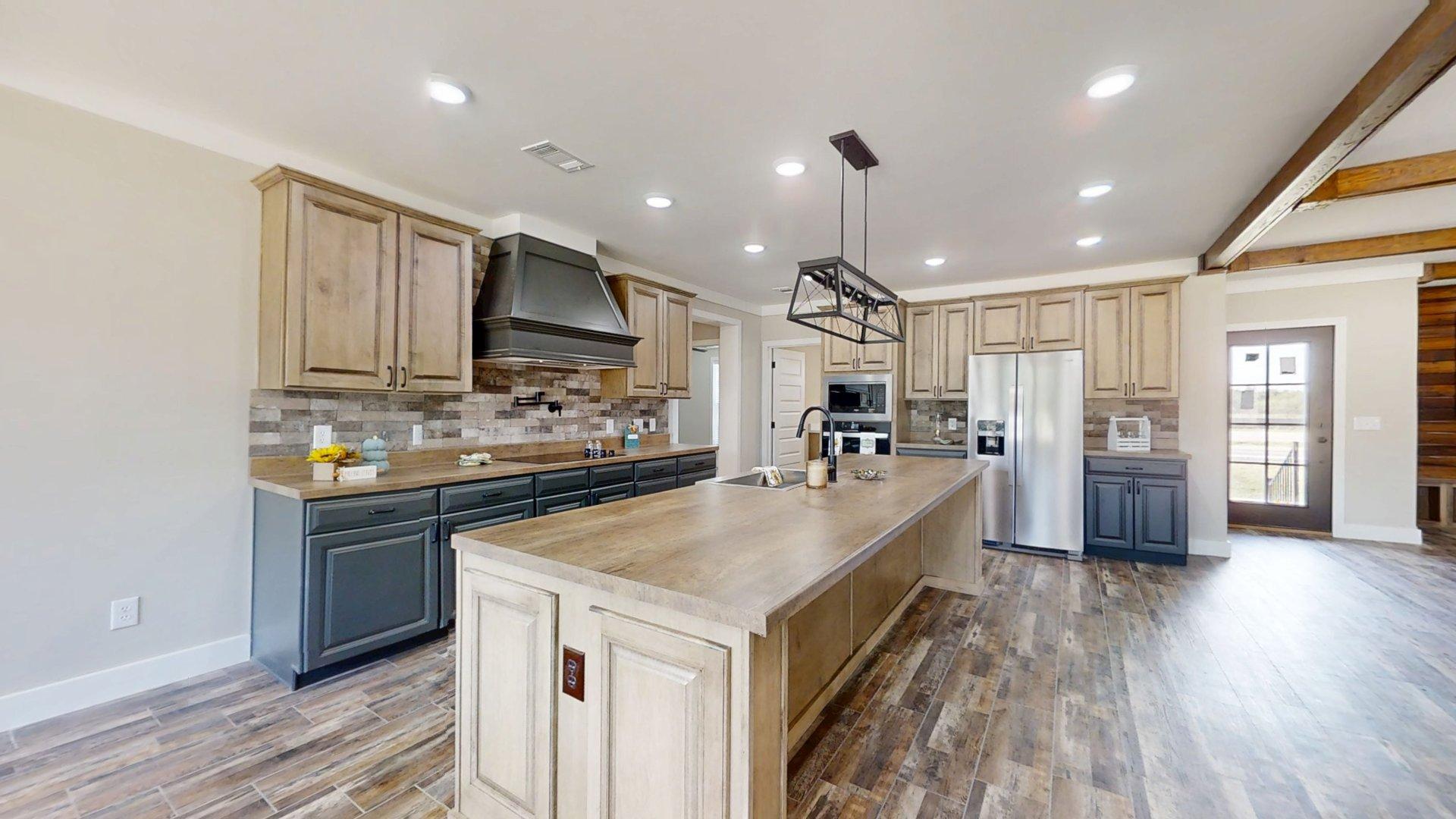 Spacious kitchen with wood floors and a large island. Includes beige cabinets, stainless steel appliances, and modern lighting. Bright, open feel.