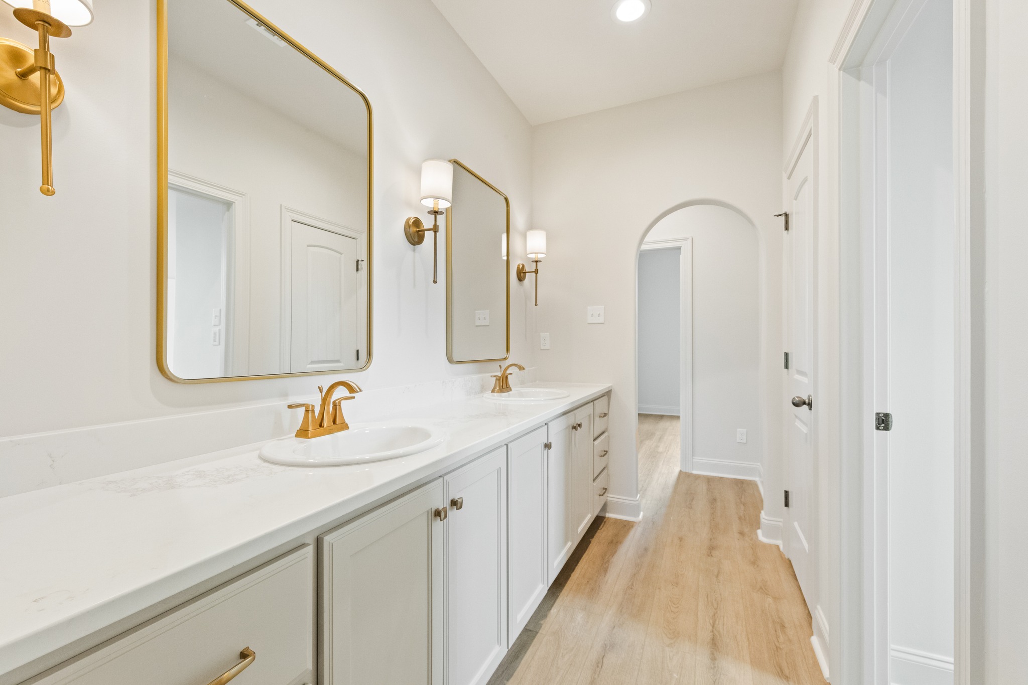 Bright bathroom with two sinks on a white vanity, gold faucets, and fixtures. Two mirrors and wall sconces create an elegant, modern look.