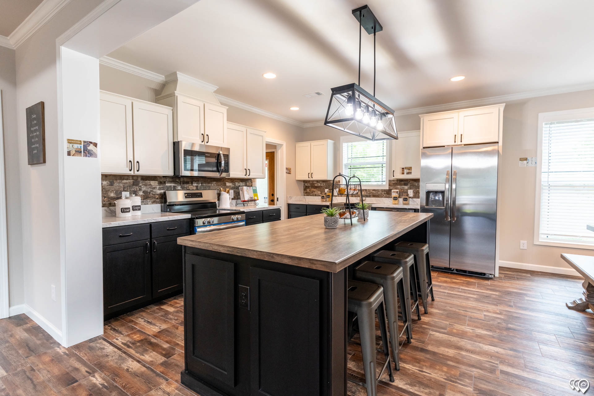 Spacious kitchen with a modern design, featuring white upper cabinets, dark lower cabinets, a large central island with bar stools, and wood flooring.