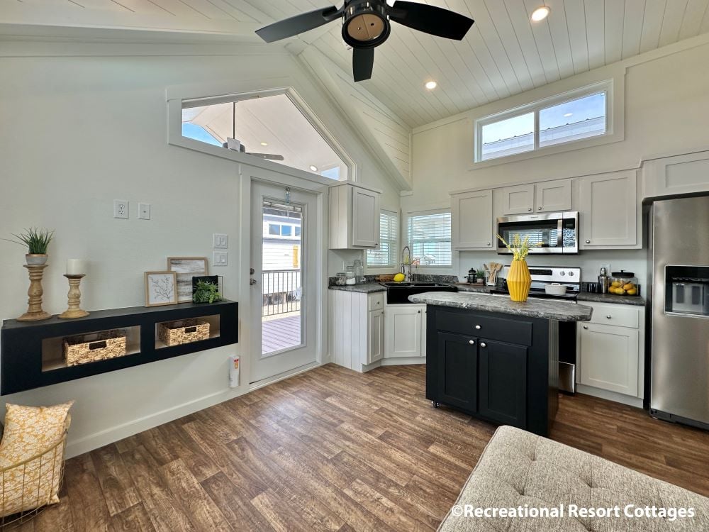 Modern kitchen with vaulted ceilings, featuring white cabinets, stainless steel appliances, and a black island. A ceiling fan and natural light create an airy feel.
