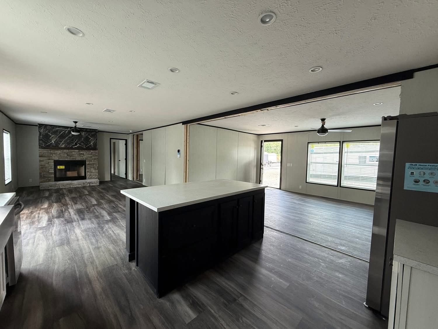 Spacious modern interior with an open floor plan, featuring a dark wood kitchen island, stone fireplace, and large windows, conveying a welcoming and airy feel.