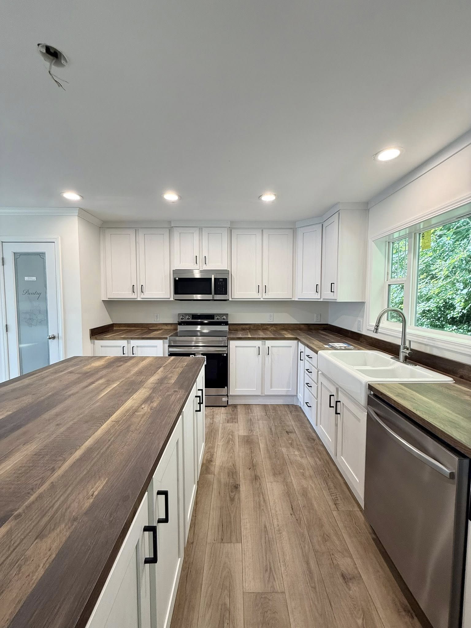 Modern kitchen with white cabinets, wood countertops, and stainless steel appliances. Bright lighting and large window create an airy feel.